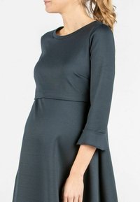 Dunkelgraues Kleid aus glattem Stoff, mit Rundhalsausschnitt, dreiviertelärmligen Ärmeln und ausgestellten Bündchen, mit einer Empire-Taillierung.