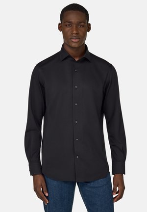 Camicia nera a maniche lunghe con chiusura a bottoni, colletto e texture liscia. Indossata con jeans blu, dal taglio classico e dettagli minimi.