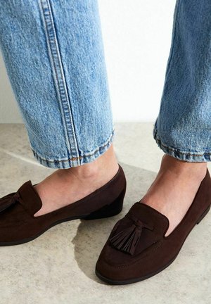 Bruine suède loafers met een kleine hak, voorzien van een kwastaccent en een klassiek ontwerp, gecombineerd met opgerolde lichtblauwe spijkerbroeken.