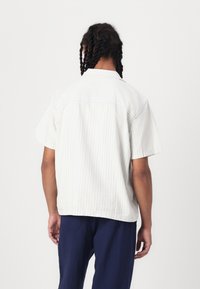Chemise à manches courtes, rayée en crème clair et bleu pâle, en coton doux, avec une coupe décontractée et un ourlet droit.