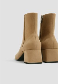 Bottines en daim marron avec un bout carré et un talon carré. Détail de fermeture éclair sur le côté intérieur ; texture lisse et design minimaliste.