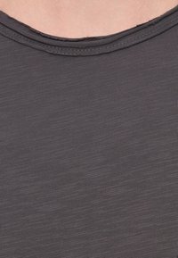 Σκούρο γκρι μπλουζάκι με κοντά μανίκια, κατασκευασμένο από μαλακό, υφασμάτινο ύφασμα με υφή, με στρογγυλή λαιμόκοψη και ακατέργαστη λεπτομέρεια στην περίμετρο της λαιμόκοψης.