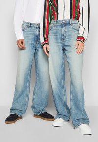 Light blue wide-leg jeans with a faded wash. One pair has traditional five pockets; the other features contrasting stitching and a relaxed fit.