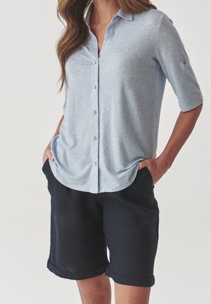 Chemise bleu clair à manches retroussées, associée à un short bleu marine foncé. La chemise a une texture douce et un motif chiné subtil.