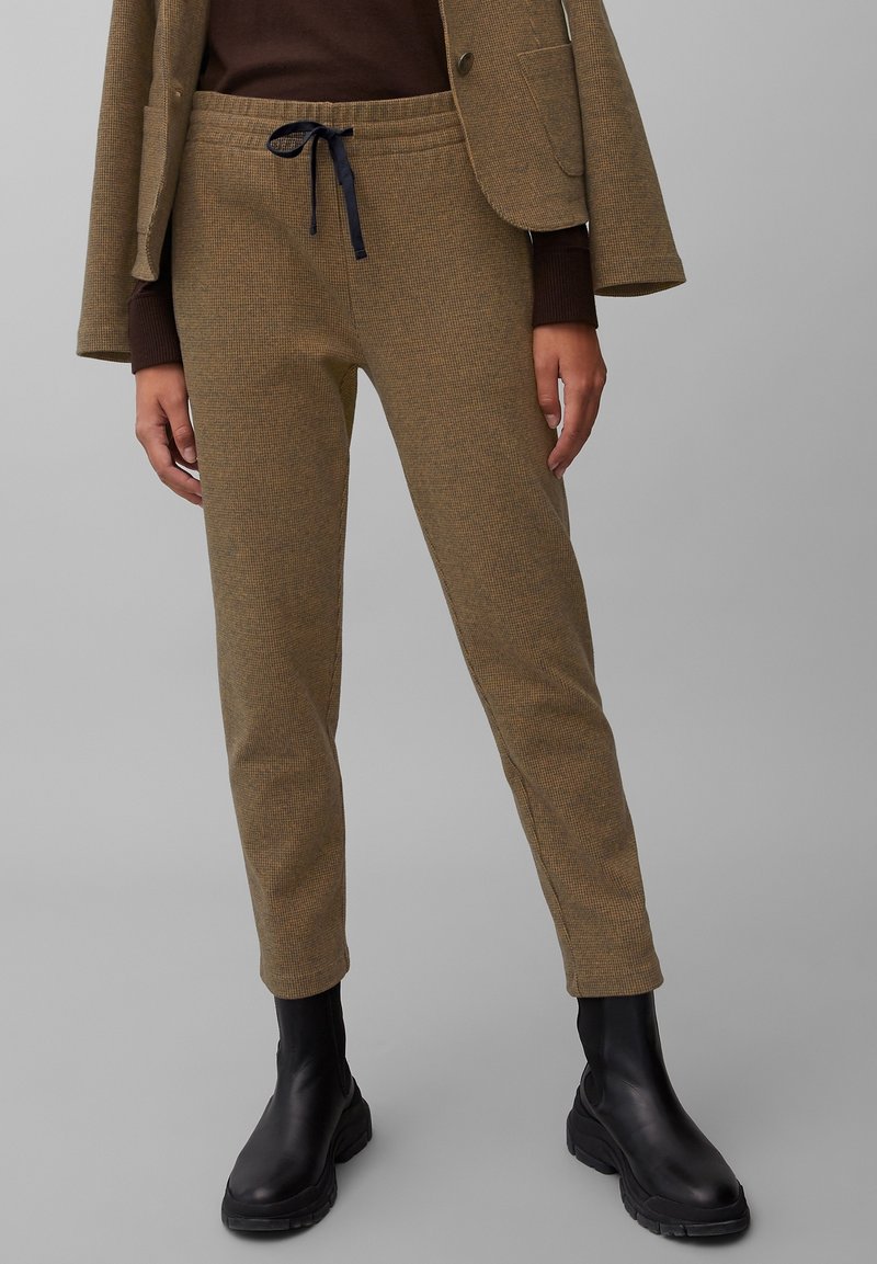Khaki textuurbroeken met een taps toelopende pasvorm, voorzien van een elastische tailleband en een marineblauwe trekkoord, gedragen met zwarte enkellaarsjes.