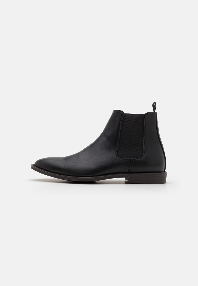 Bottine Chelsea en cuir noir avec panneau latéral élastique et languette de traction sur fond blanc, vue de côté extérieur.