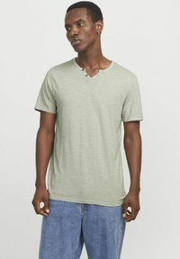 Lysegrøn bomulds t-shirt med korte ærmer og V-hals, der har to dekorative knapper ved halsudskæringen og et blødt, tekstureret stof.