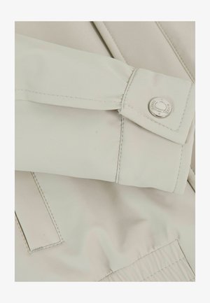 Rękaw jasnobeżowej kurtki z mankietem zabezpieczonym srebrnym zatrzaskiem z logo "Reiss" i widocznymi pionowymi detalami szwów.