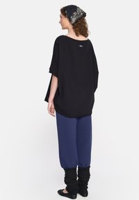 Czarny, oversize'owy top z krótkimi rękawami, zestawiony z niebieskimi spodniami dresowymi i czarnymi, marszczonymi getrami, uzupełniony wzorzystym czarnym szalikiem.