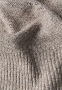 Ljusbrun texturerad tyg med en mjuk, fluffig yta; har ribbat detalj vid kanten och ett subtilt, vävt mönster genom hela.