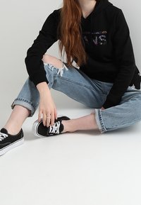 Czarna bluza z kapturem z graficznym nadrukiem, zestawiona z podartymi jasnoniebieskimi dżinsami i czarnymi tenisówkami z białymi sznurowadłami.