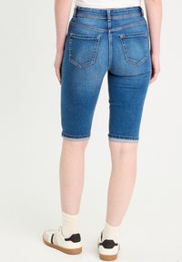 Niebieskie szorty bermudy z denimu w średnim odcieniu, o dopasowanym kroju, z podwiniętym dołem i dwiema tylnymi kieszeniami. Posiadają wysoki stan oraz fakturowany materiał.
