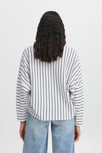 Weißer, übergroßer Pullover mit navyfarbenen vertikalen Streifen, mit einem lockeren Schnitt, abgerundetem Saum und gerippten Bündchen. Casual Denim-Hosen runden das Outfit ab.