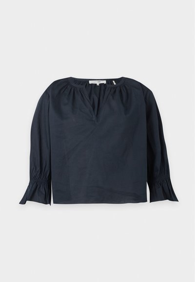 Blouse bleu marine à manches longues avec encolure froncée, légère découpe en V, et poignets évasés avec détail élastique sur fond clair.