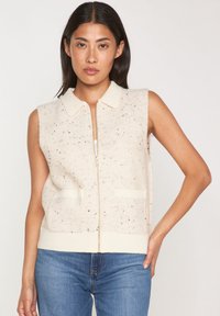 Gilet sans manches de couleur crème avec fermeture éclair sur le devant, deux poches avant et un col ; fabriqué en tissu tricoté moucheté.