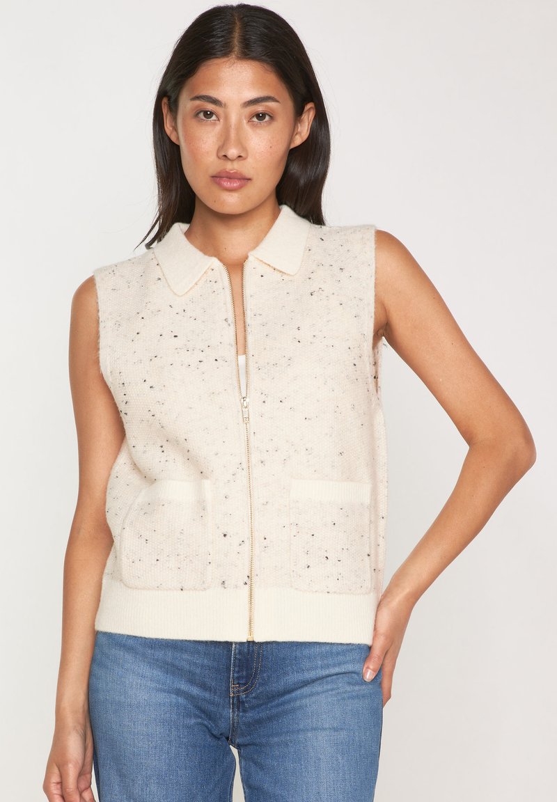 Gilet sans manches de couleur crème avec fermeture éclair sur le devant, deux poches avant et un col ; fabriqué en tissu tricoté moucheté.