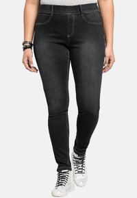 Ohuet mustat farkut, joissa on sileä pinta, hienovaraiset ompelukoristeet ja etutaskut. Yhdistetty kimaltaviin hopeisiin lenkkareihin.