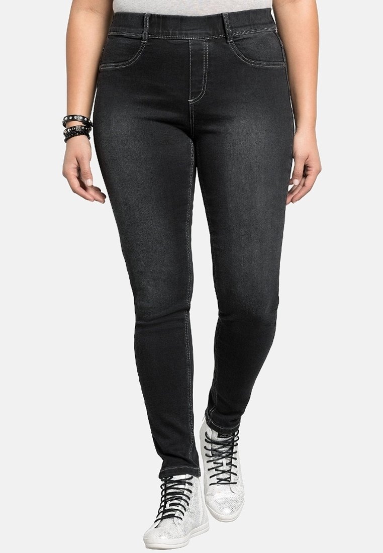 Ohuet mustat farkut, joissa on sileä pinta, hienovaraiset ompelukoristeet ja etutaskut. Yhdistetty kimaltaviin hopeisiin lenkkareihin.