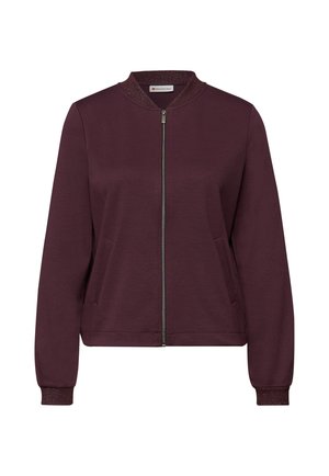 Bordeauxrode jas met ritssluiting, ronde kraag, gestructureerde manchetten en zijzakken. Gemaakt van zachte stof, met een metalen ritsdetail.