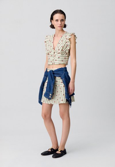 Top corto con maniche a volant a righe crema e verde, abbinato a una gonna a righe. Giacca di denim legata in vita, scarpe nere basse.