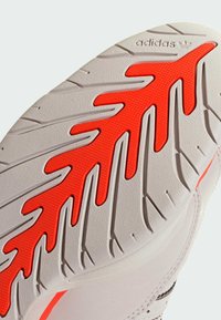 Schuhsohle mit weißer, strukturierter Basis und markanten roten Gummidetails in Blattmuster, versehen mit tiefen Rillen für besseren Halt.