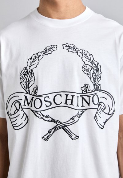 T-shirt en coton blanc avec un design graphique noir représentant une couronne de laurier et des branches croisées, avec le texte "Moschino" dans une bannière en forme de ruban.