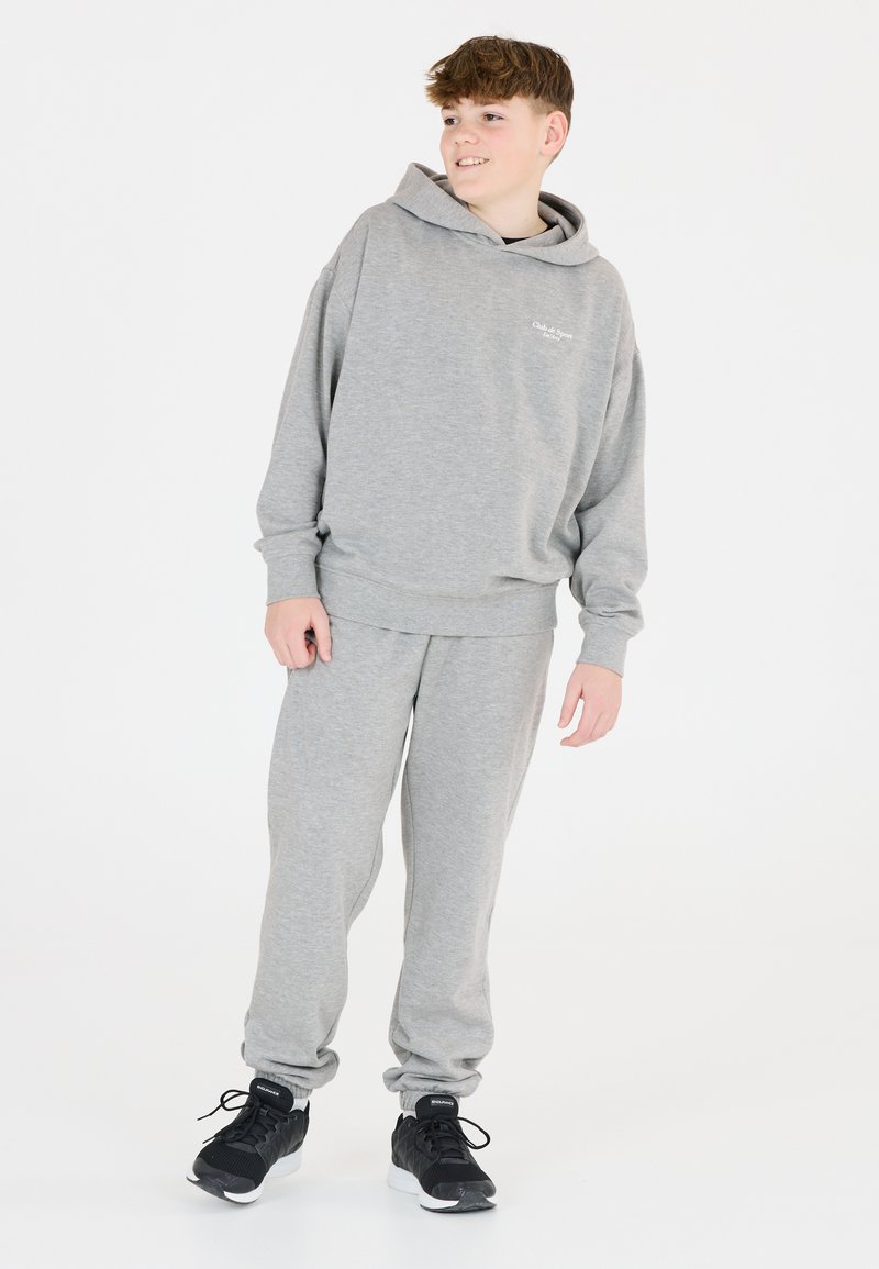 Grau Hoodie und passende Jogginghose aus weichem Stoff, mit lockerer Passform und gerippten Bündchen, kombiniert mit schwarzen Sportschuhen.