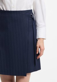 Marineblauwe rok met krijtstreep, voorzien van een overslagontwerp, zijsluiting met een ronde metalen detail en een gladde stoftextuur.