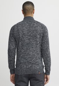 Maglione pullover grigio scuro con colletto alto, motivo a maglia testurizzata, maniche lunghe e orlo a costine. Presenta una piccola etichetta con logo marrone.