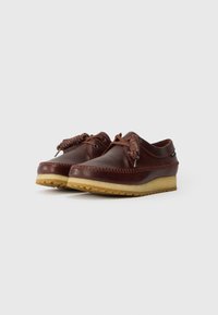 Sapatos de couro castanho com atacadores trançados, apresentando um design cosido e uma sola de borracha de cor clara com uma superfície texturizada.