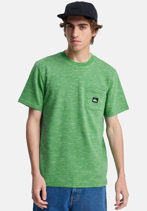 Grün gestreiftes T-Shirt mit kurzen Ärmeln, Rundhalsausschnitt und einer Brusttasche mit einem schwarzen Logo-Patch. Wird mit blauen Jeans getragen.