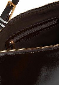 Innenansicht einer dunkelbraunen Ledertasche mit goldenem Reißverschluss, innerer Reißverschlusstasche, Stofffutter und verstellbarem Riemen mit goldener Schnalle.