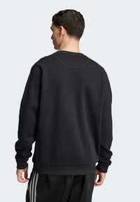 Felpa nera con scollo rotondo, maniche raglan e polsini a costine. Texture liscia e design minimalista. Indossata con pantaloni neri.