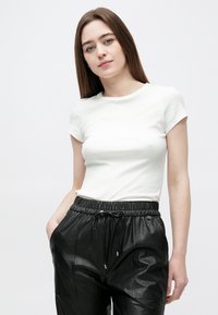 Valge soonikkoega lühikeste varrukatega t-särk mustade nahast jookspükstega, millel on elastne vöökoht ja nööriga detail.