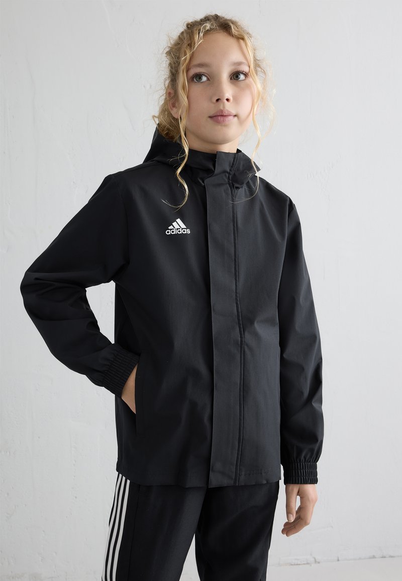 Veste imperméable noire avec fermeture éclair à l'avant, poignets élastiques et capuche ajustable. Présente le logo Adidas en blanc sur la poitrine gauche.