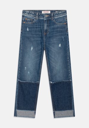 Jean en denim bleu à coupe droite, présentant des patchs déchirés, un mélange de textures et des ourlets retroussés. Design classique à cinq poches.