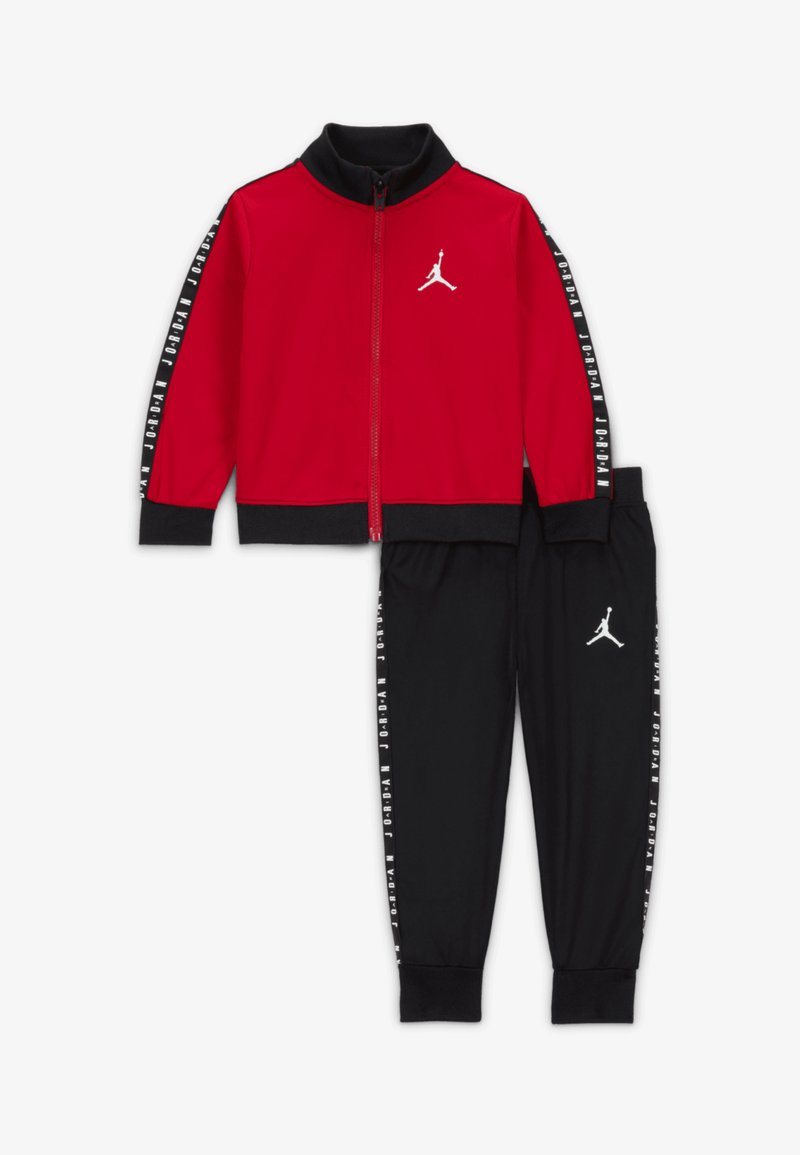 Červená bunda na zips s čiernymi detailmi a logom Jordan. Čierne nohavice s bielymi bočnými pruhmi nesúcimi názov značky a logo.