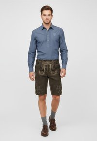 Dark brown lederhosen with decorative stitching and gold accents, paired with a blue button-up shirt and gray socks. Brown shoes complete the look.