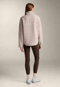 Fleece pullover in zacht beige met een hoge kraag, ontspannen pasvorm en lange mouwen. Draag het met bruine leggings en lichte sneakers.