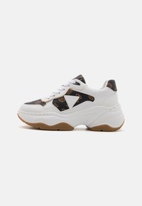 White sneakers with a textured black fabric featuring a circular pattern. Thick sole with a gum outsole and a prominent logo on the side.