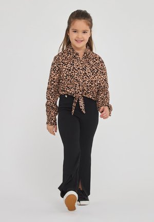Camicia a bottoni con stampa leopardata e davanti legato, abbinata a pantaloni neri a palazzo con spacchi e sneakers nere con suola bianca.