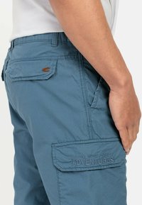 Blå cargo shorts lavet af tekstureret stof, med sidelommer og baglommer, samt et "adventures" slogan broderet på sidelommen.
