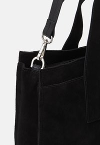 Zwarte suède tote bag met een gladde textuur, voorzien van een zilveren metalen sluiting en een verstelbare schouderband. Inclusief een buitentas.