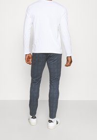 Long-sleeve white shirt paired with gray check-patterned trousers and white sneakers with black accents; focus on fit and material.