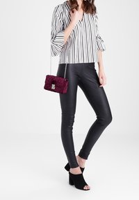 Blusa rayada en blanco y negro con mangas sueltas, combinada con pantalones de cuero negro ajustados y un bolso burdeos acolchado con cadena.