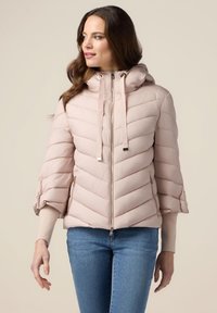 Polstret pink jakke med hætte, der har zigzag quiltet design, sølv lynlås og strikkede manchetter. Sidelommer med lynlåslukning.