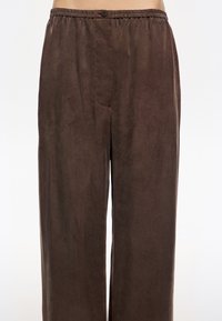 Pruunid laiad püksid, mis on valmistatud pehmest ja siledast kangast. Omavad elastset vööd nööpiga detailiga ning nähtavaid taskuid ei ole.
