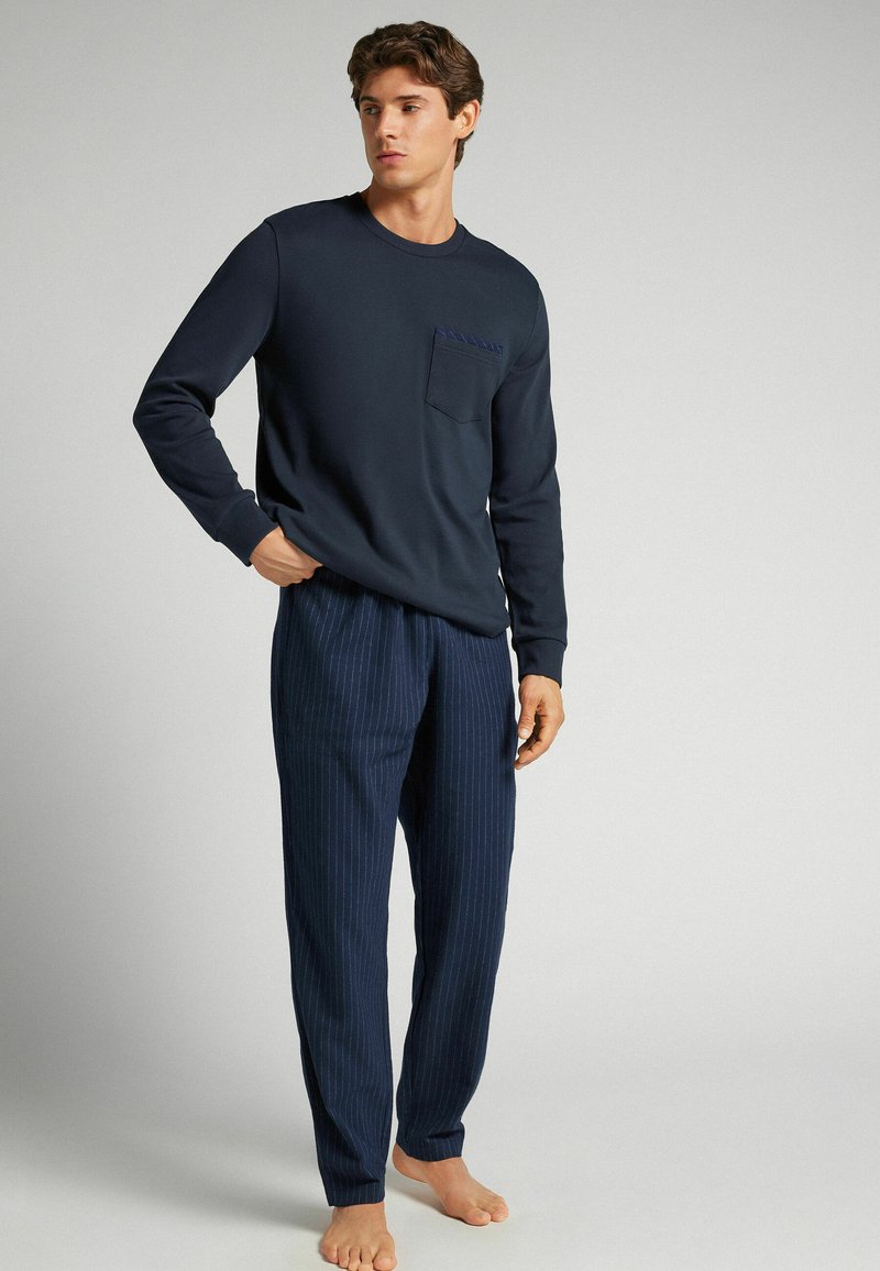 Camisa de manga larga azul marino con un bolsillo en el pecho, combinada con pantalones de patrón rayado azul marino. El material parece suave, la textura es lisa.