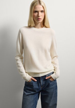 Pull en tricot de couleur crème, avec un col rond et des poignets côtelés, associé à un jean en denim bleu ample.