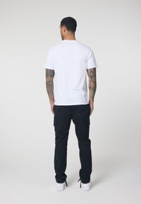 White short-sleeve t-shirt with crew neck, paired with black cargo pants featuring side pockets and fitted cuffs, worn with white sneakers.